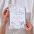 Baby shower invitation with fox and rabbit design held by hands against a neutral background