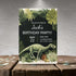 Birthday party invitation with dinosaur and tropical plants on a wooden surface.