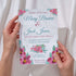 Wedding invitation card with floral design held by hands against a white background