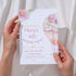Hand holding a birthday party invitation with pink balloons and flowers.