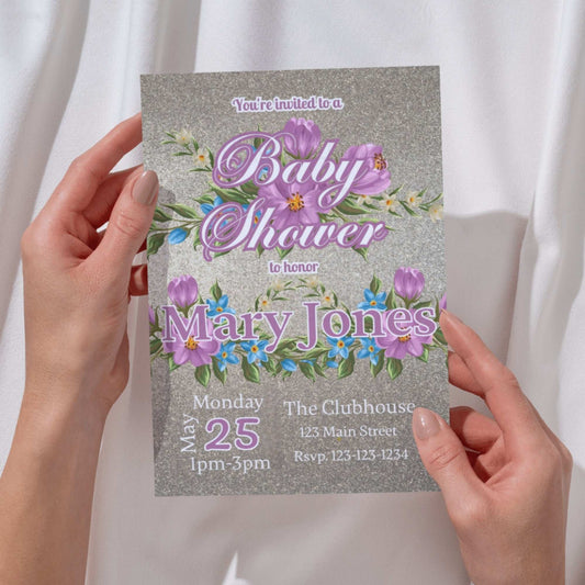 Baby shower invitation with floral design held by hands against a white background
