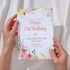 Hand holding a birthday invitation card with floral design