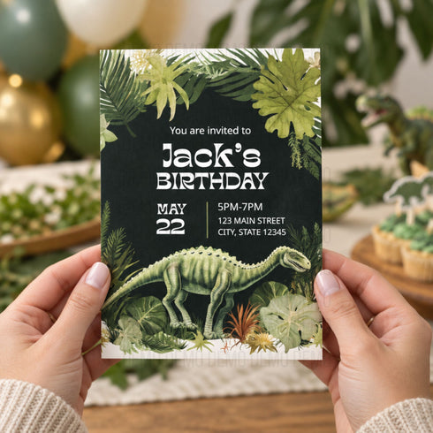 A person holds a dinosaur-themed birthday invitation card in front of a blurred festive background with balloons and plants. The card features a dark jungle design with a green dinosaur illustration and white event text reading 'Jack's Birthday' and 'May 22'.