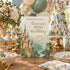 A printed birthday invitation card featuring a watercolor-style castle illustration and the text 'Emma's 10th Birthday,' styled on a party table with cupcakes, plates, balloons, and a matching castle cake in the background.