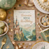 A styled flat-lay of a custom birthday invitation card featuring a fairytale castle illustration. The card is surrounded by matching green and gold party supplies, including paper plates, cups, macarons, a gold fork, and decorative confetti, all arranged on a rustic wooden table.