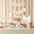 A coordinated autumn baby shower table decoration set with printed signs, cupcake toppers, a photo frame, place cards, and pumpkin accents arranged on a draped beige fabric backdrop.