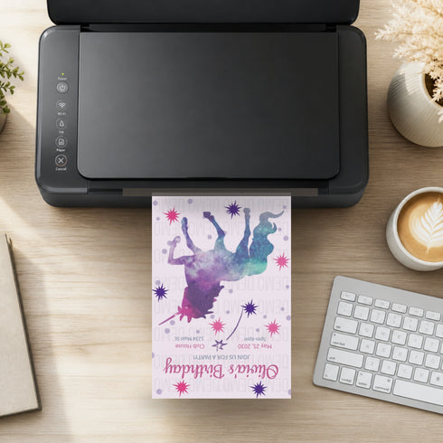 A black printer sits on a wooden desk with a colorful birthday invitation card emerging from the front. The card features a purple and blue watercolor silhouette of a person with stars and the text 'Olivia's Birthday'.
