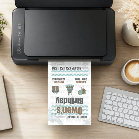 A black desktop printer on a light wood desk, printing a personalized birthday invitation card. The card features a white background with blue wavy lines, black text, and small illustrations of a pair of boots, a patterned top hat, and a silver teapot.