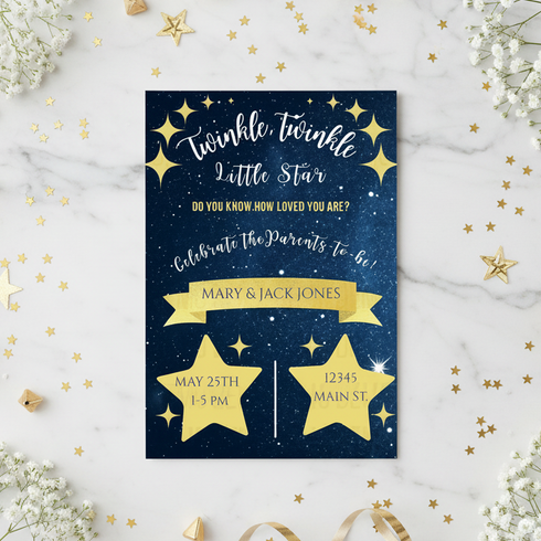 A personalized baby shower invitation card with a navy blue starry space background and gold foil stars, placed on a white marble surface with gold star confetti and baby's breath flowers.