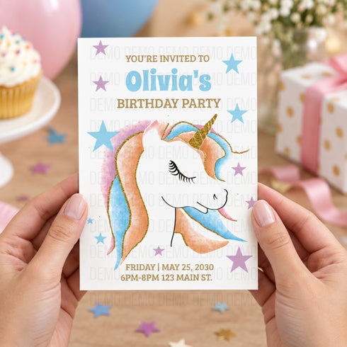 A person holds a unicorn-themed birthday party invitation card. The card features a pastel watercolor-style unicorn with pink, blue, and gold accents, along with blue and gold stars.