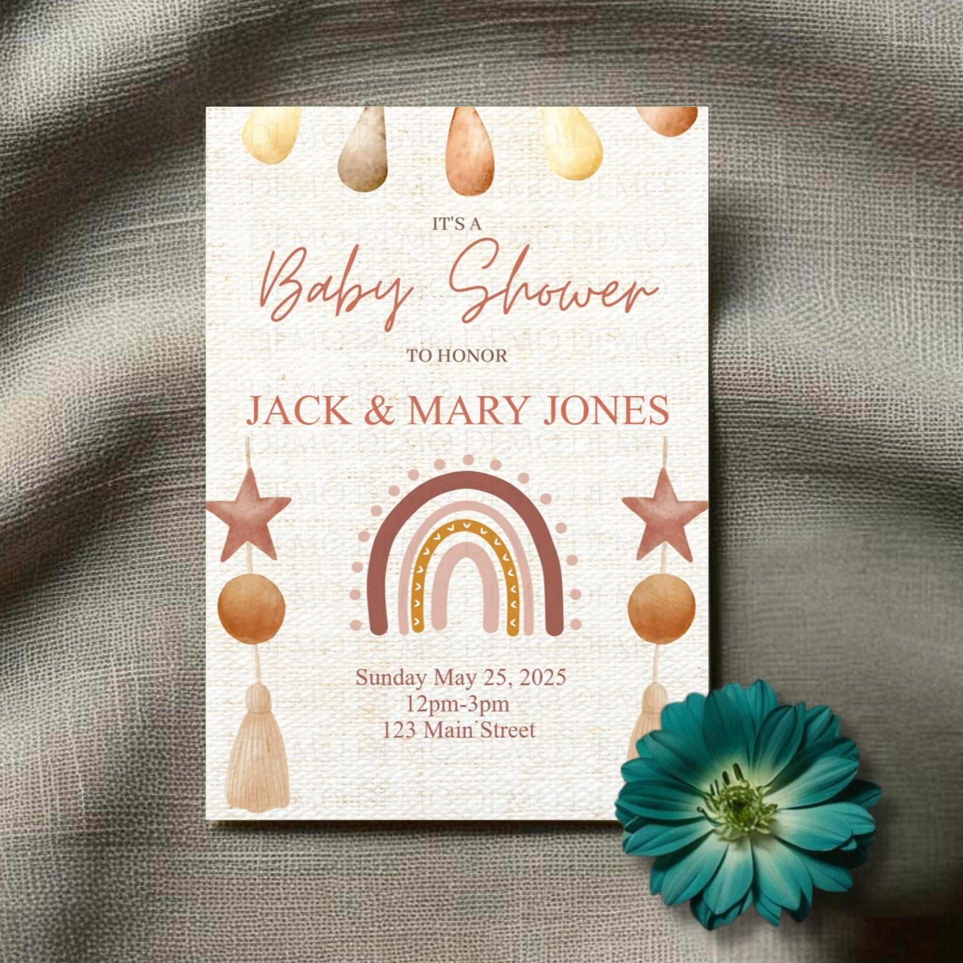 Baby shower invitation with rainbow, stars, and teardrop decorations on a textured surface with a blue flower.