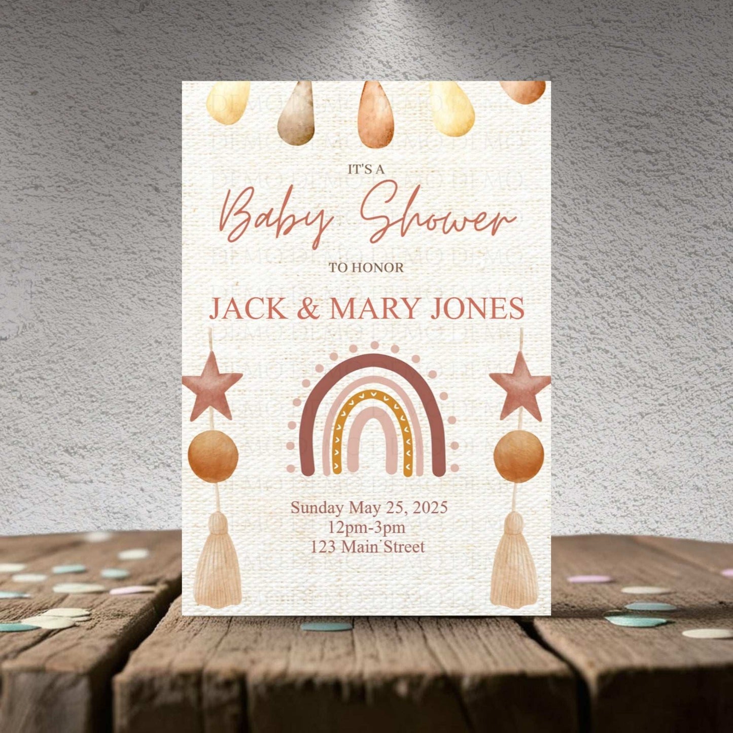 Baby shower invitation with rainbow, stars, and hanging elements on a textured surface.