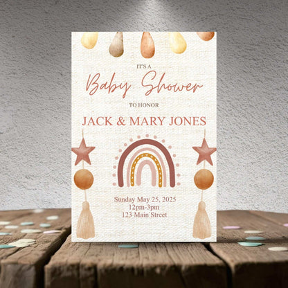 Baby shower invitation with rainbow, stars, and hanging elements on a textured surface.