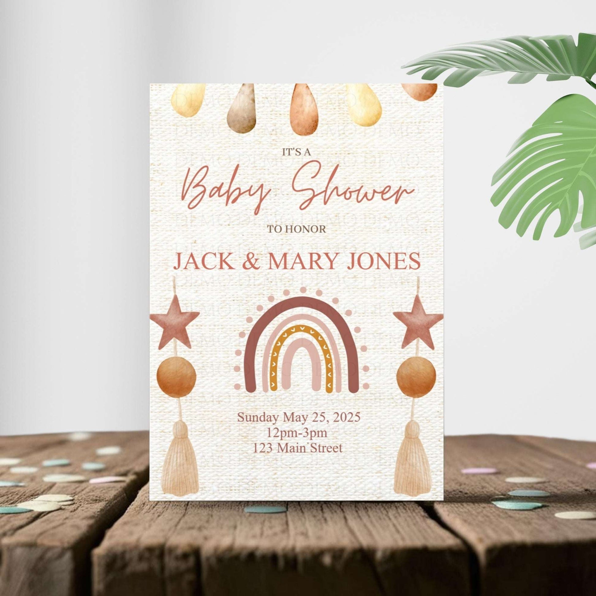 Baby shower invitation with rainbow, stars, and tassels on a wooden surface.