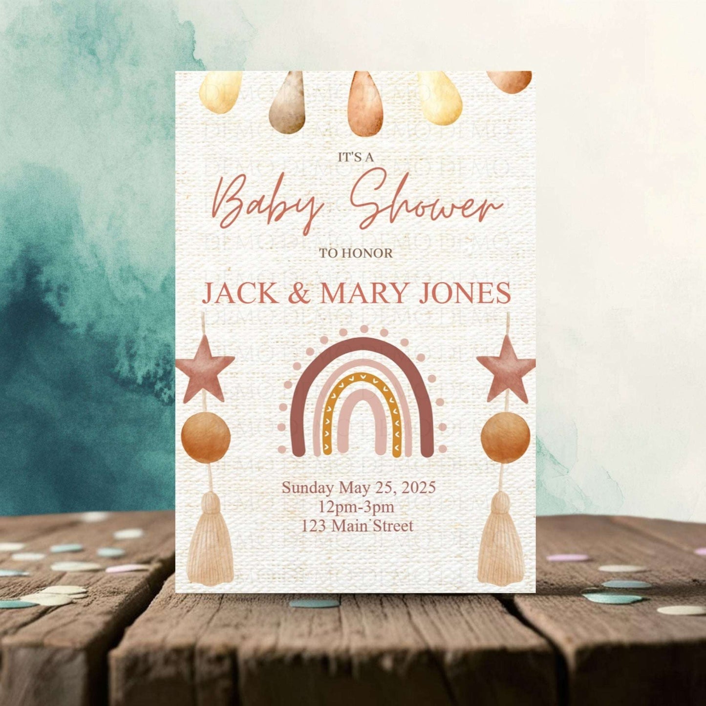 Baby shower invitation with rainbow, stars, and hanging elements on a wooden surface.