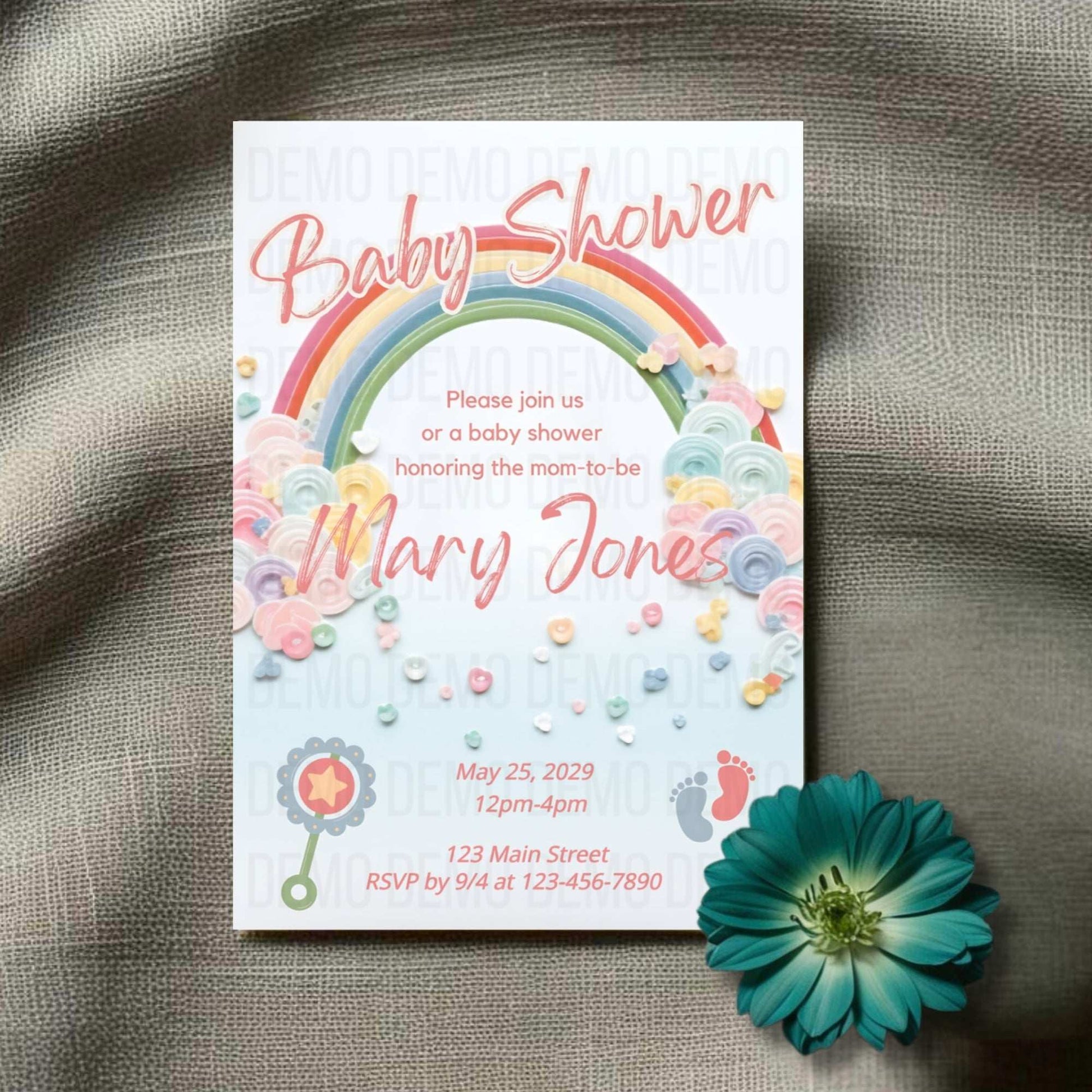 Baby shower invitation with rainbow and flowers on a textured surface with a teal flower.