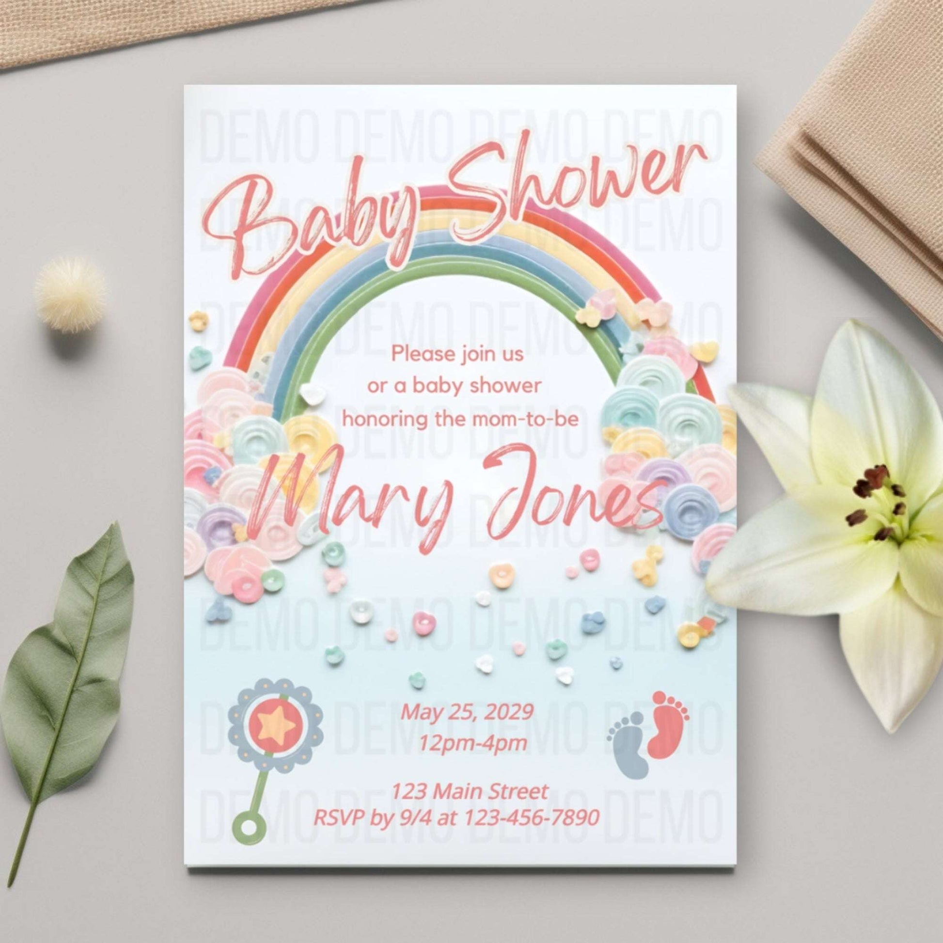 Baby shower invitation with rainbow and floral design on a light surface with flowers and leaves.