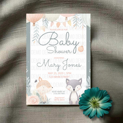 Baby shower invitation with fox and floral design on a textured surface with a flower.
