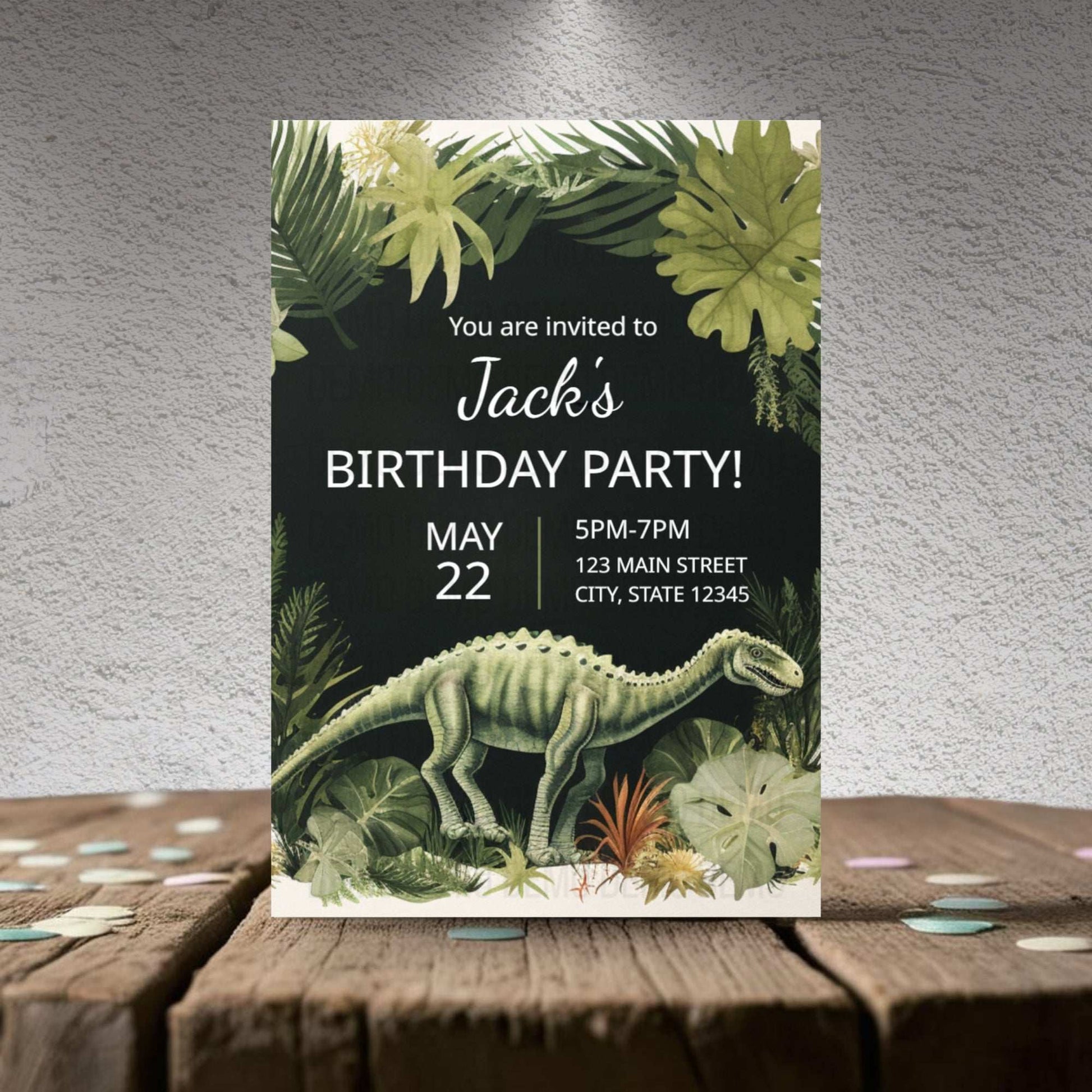Birthday party invitation with dinosaur and tropical plants on a wooden surface.