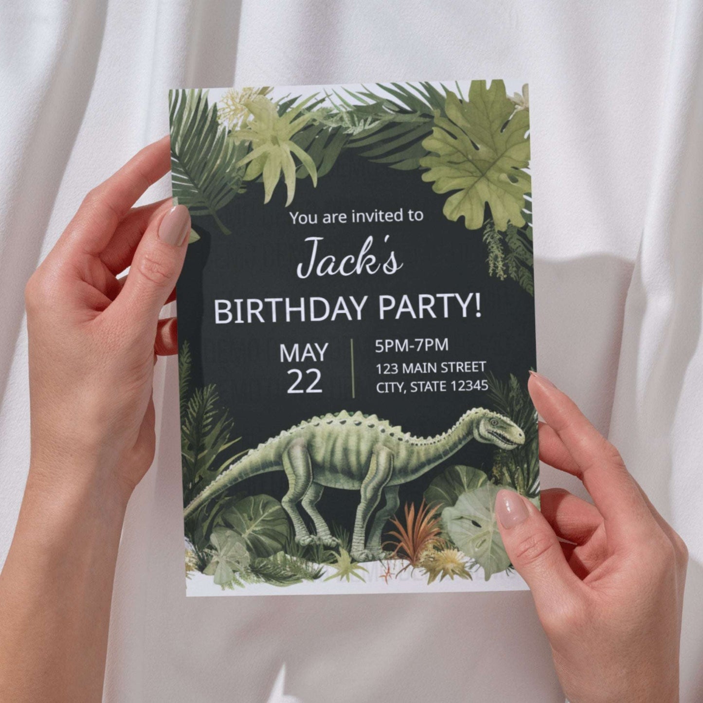 Birthday party invitation with dinosaur and foliage design held by hands against a white curtain background