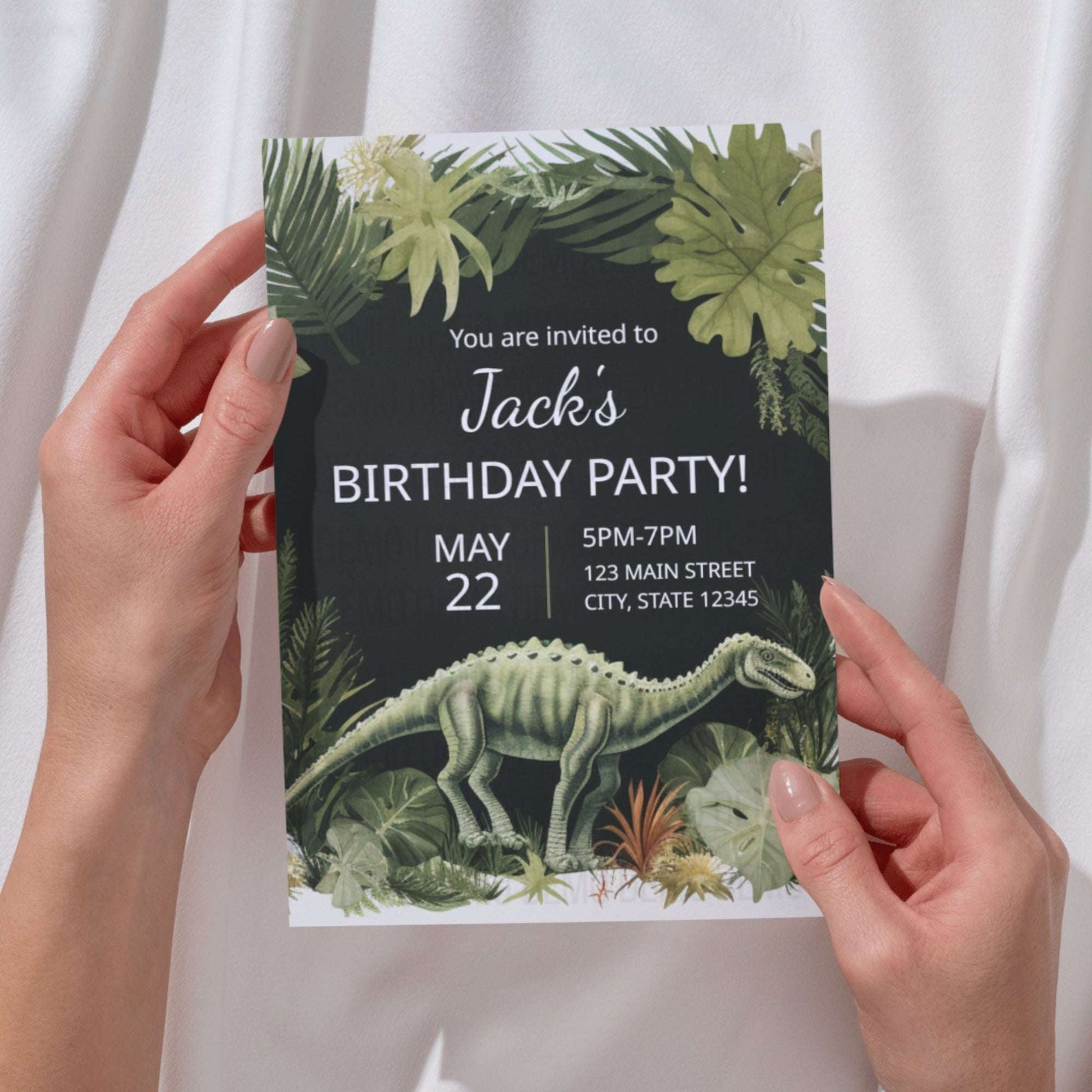 Birthday party invitation with dinosaur and foliage design held by hands against a white curtain background