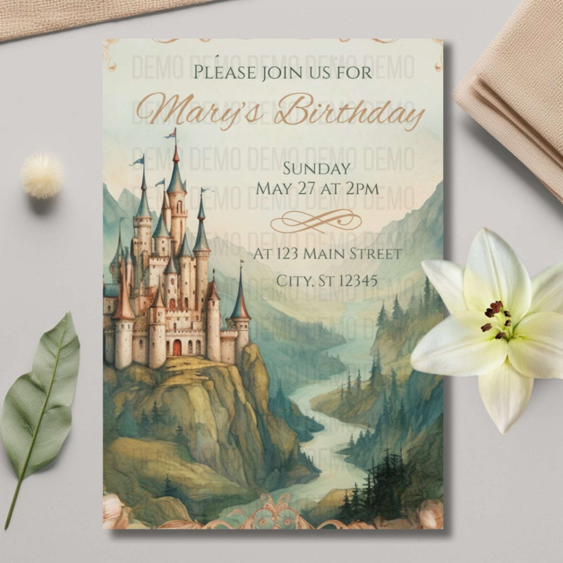 Birthday invitation card with castle design on a light gray surface with a flower and leaves.