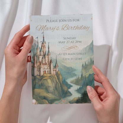 Hand holding a birthday invitation card with a castle design on a white background