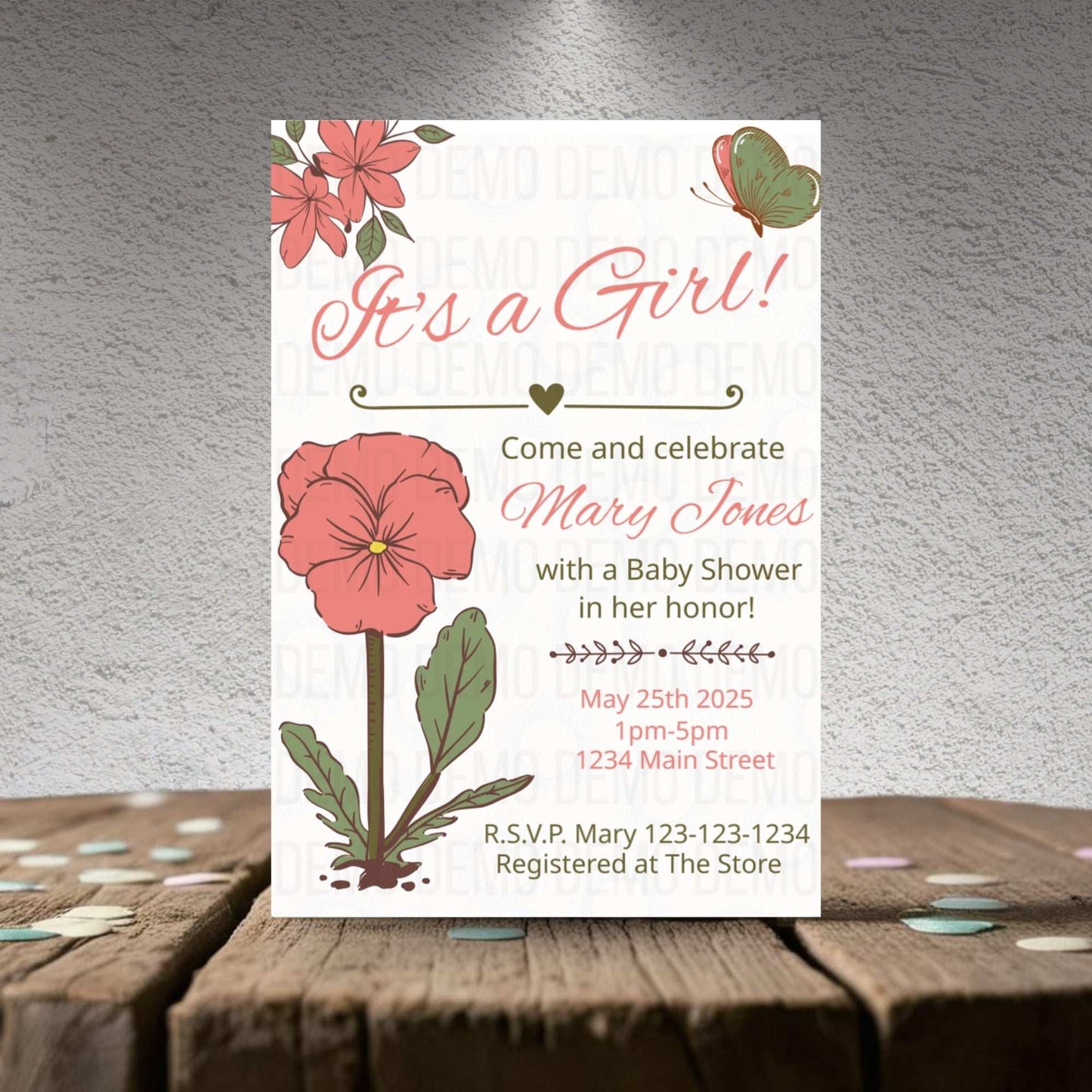 Baby shower invitation for a girl with floral design on a wooden surface.