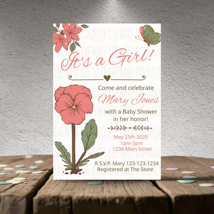 Baby shower invitation for a girl with floral design on a wooden surface.