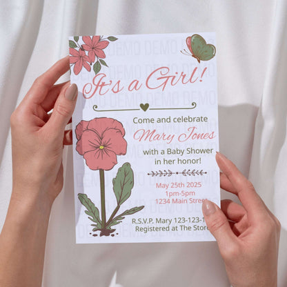 Baby shower invitation with floral design held by hands against a white background