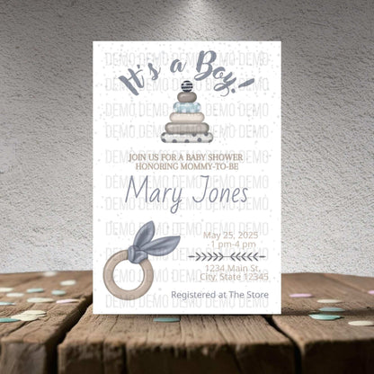 Baby shower invitation for a boy with cake and baby bootie design on a textured surface.