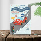 Children's birthday party invitation with a race car theme on a wooden surface.