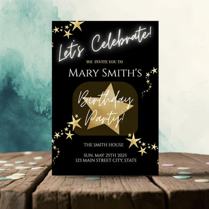 Birthday party invitation card with gold star design on a black background, placed on a wooden surface with confetti.