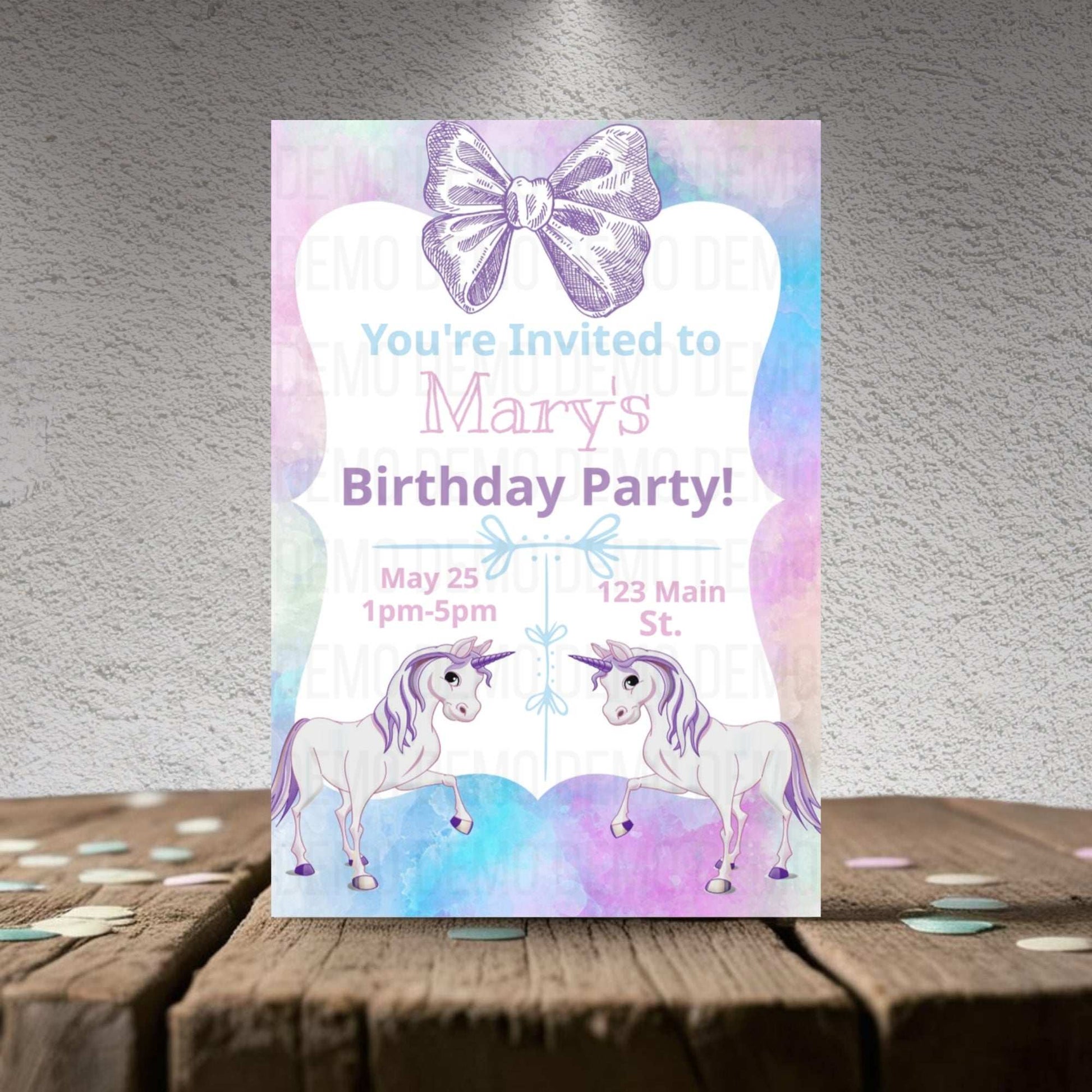 Birthday party invitation with unicorns and a bow on a wooden surface.