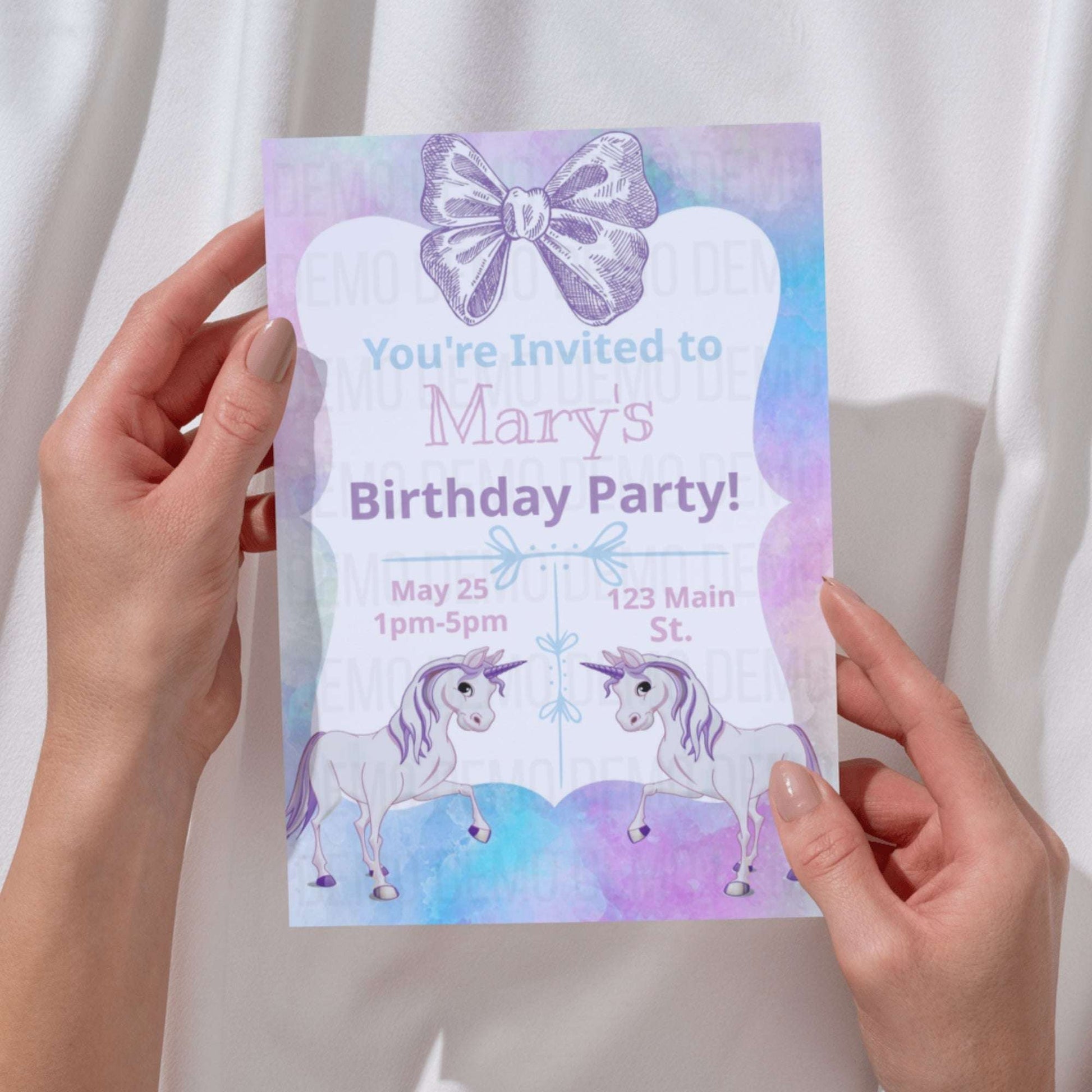 Hand holding a birthday party invitation with unicorns and a bow design.