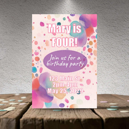 Birthday party invitation with colorful polka dots on a wooden surface.