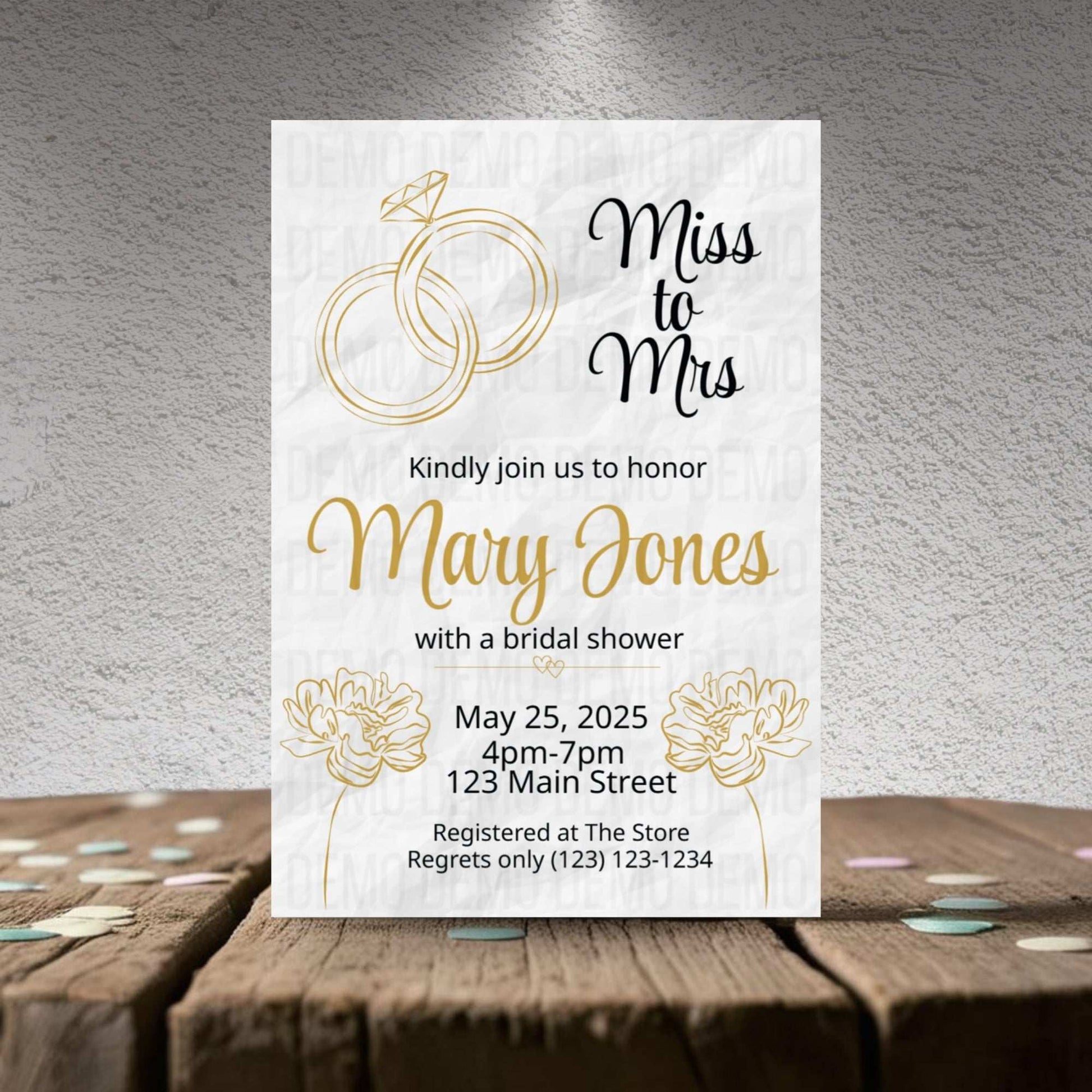 Bridal shower invitation with gold rings and floral elements on a textured surface.