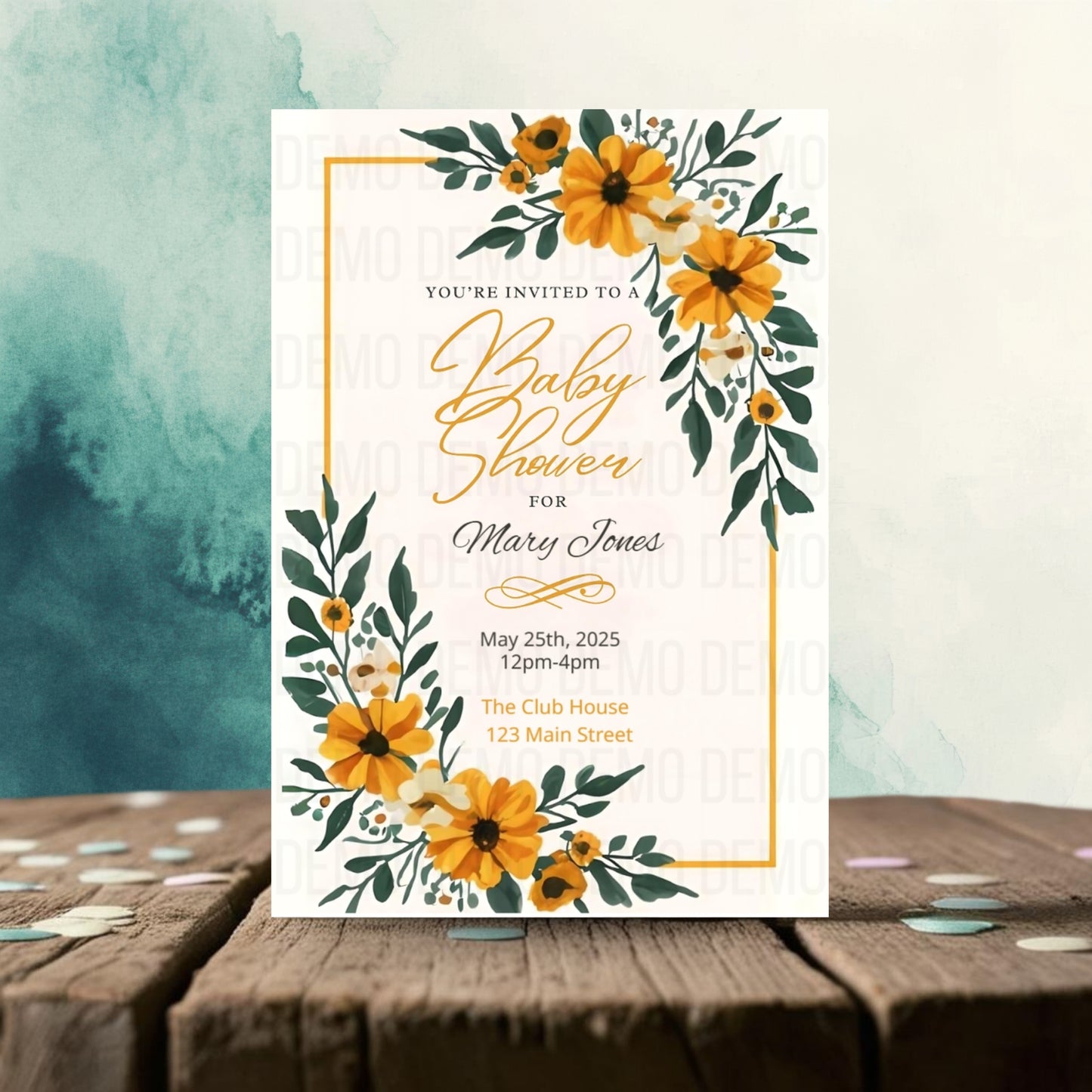 Baby shower invitation with yellow flowers and green leaves on a wooden surface.