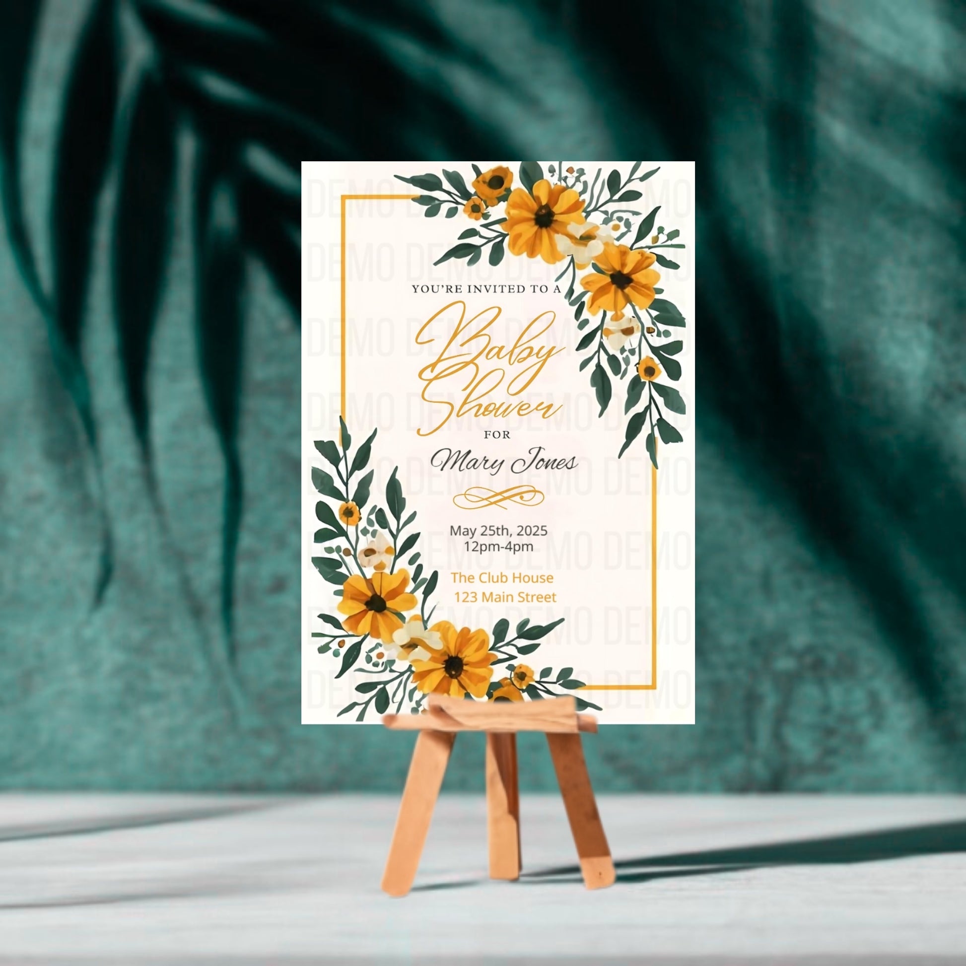 Baby shower invitation with yellow flowers on a white background, displayed on a small easel against a green leafy background.